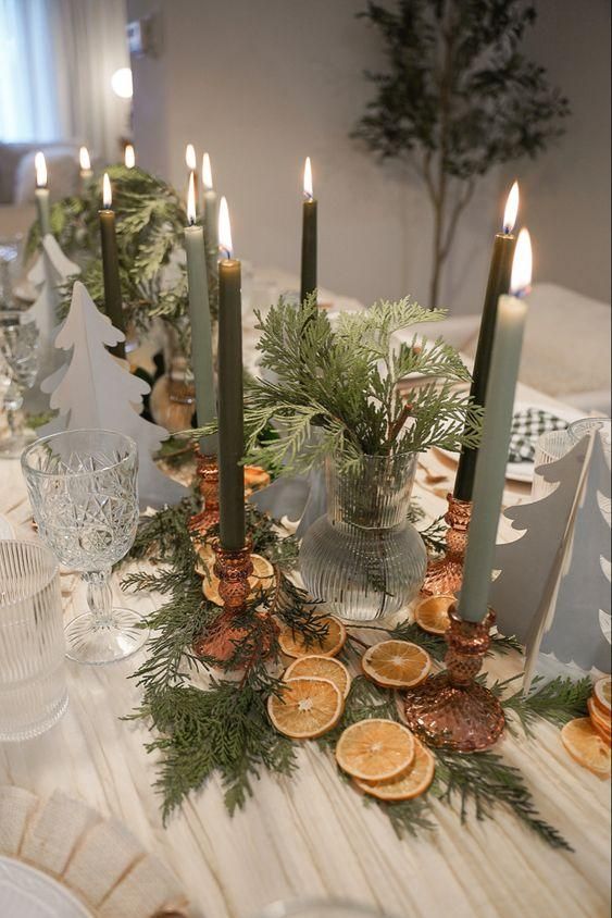 Green Christmas candles on a table decorated with dried lemon slices and pine foliage